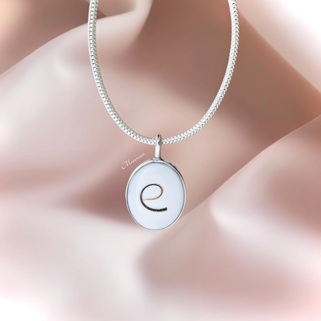 Zilveren haarlok sieraad. Het haarlokje werd gevormd in de letter 'e'. Formaat: 8x10mm